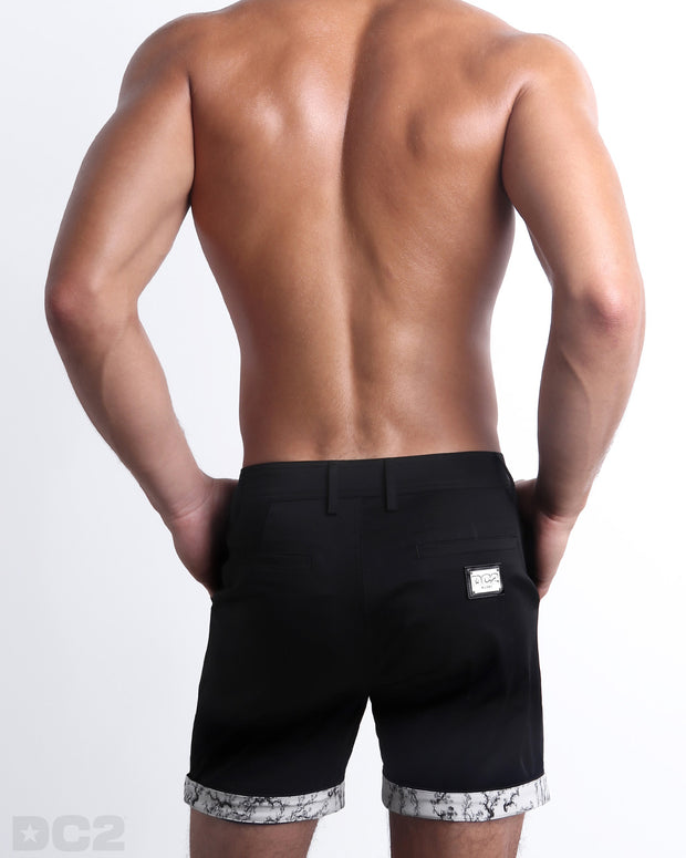 Back view of a model wearing woven twill cotton chino shorts in a black color for men. These premium quality swimwear bottoms are DC2 by BANG! Clothes, a men’s beachwear brand from Miami.