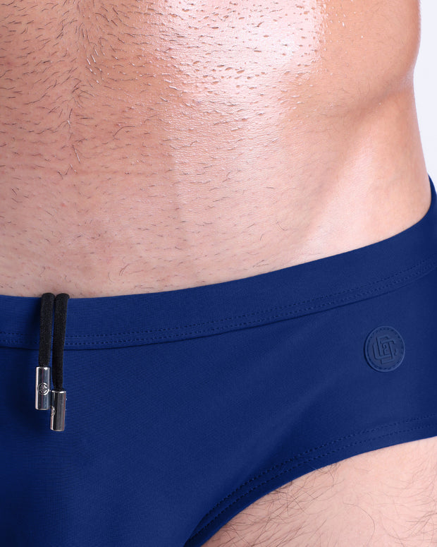 Close-up view of the BLUE BY THE OCEAN men’s drawstring briefs showing black cord with custom branded metallic silver cord ends, and matching custom eyelet trims in silver.