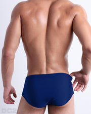 Back view of male model wearing the BLUE BY THE OCEAN beach Brazilian Sunga swimwear for men by BANG! Miami in a solid ocen blue color.