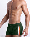 Side view of the BRAVE GREEN for men’s Summer Mini Shorts. This swimsuit is in a solid green color with orange and white colored stripes on the side designed by DC2 a brand based in Miami.