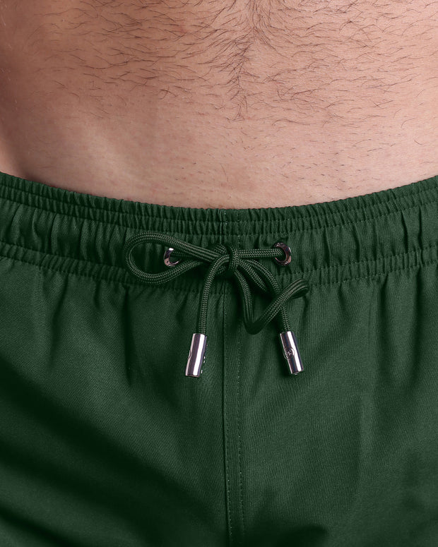 Close-up view of the BRAVE GREEN men’s summer shorts, showing green cord with custom branded silver cord ends, and matching custom eyelet trims in silver.