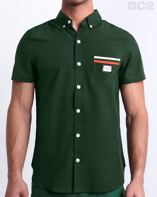 Male model wearing BRAVE GREEN men’s sleeveless stretch shirt. A premium quality top in a solid green color with orange and white stripes on the pocket, a men’s beachwear brand from Miami.