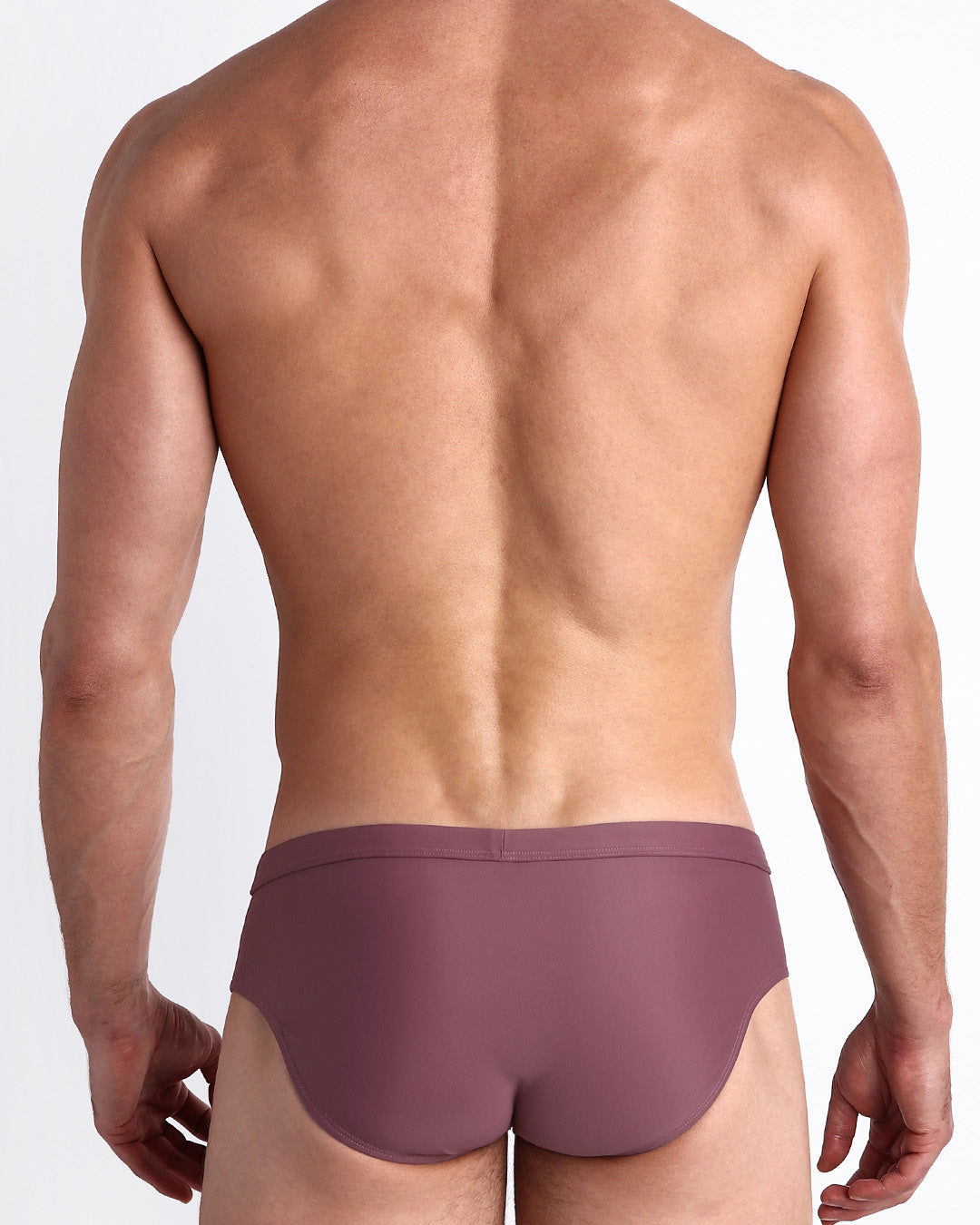 Back view of a male model wearing men’s swim briefs in BUST A MAUVE a solid light purple wine color made with Italian-made Vita By Carvico Econyl Nylon by the Bang! Clothes brand of men's beachwear.