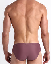 Back view of a male model wearing men’s swim briefs in BUST A MAUVE a solid light purple wine color made with Italian-made Vita By Carvico Econyl Nylon by the Bang! Clothes brand of men's beachwear.