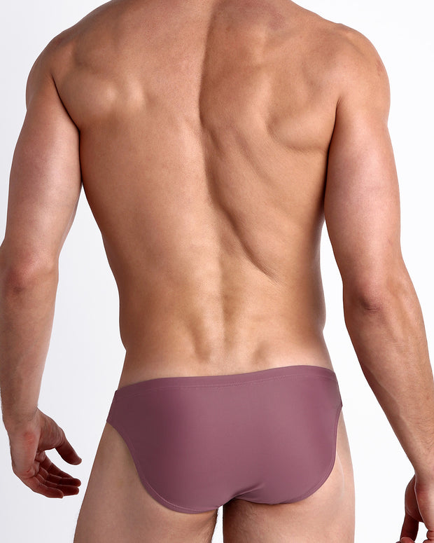 Back view of male model wearing the BUST A MAUVE beach mini-briefs made with Italian-made Vita By Carvico Econyl Nylon for men by BANG! Miami in a solid mauve light purple color.