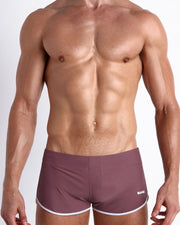 Frontal view of a sexy male model wearing the BUST A MAUVE men’s swimsuit in a light plum color by the Bang! Menswear brand from Miami.