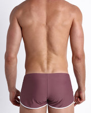 Back view of a male model wearing BUST A MAUVE men’s swim shorts in a solid light purple wine color made with Italian-made Vita By Carvico Econyl Nylon by the Bang! Clothes brand of men's beachwear.