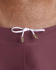 Close-up view of men’s summer beach shorts by BANG! clothing brand, showing white cord with custom branded golden cord ends, and matching custom eyelet trims in gold.