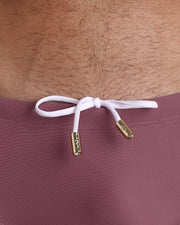 Close-up view of the BUST A MAUVE Swim Sunga mens swimsuit a solid mauve color with white internal drawstring cord showing custom branded golden buttons by BANG! clothing brand.