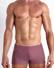 Frontal view of a sexy male model wearing men’s BUST A MAUVE swimsuit with mini pockets in a light plum color made with Italian-made Vita By Carvico Econyl Nylon by the Bang! Menswear brand from Miami.