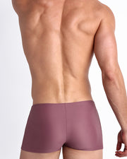 Side view of a masculine model wearing men’s swimsuit compression shorts in BUST A MAUVE a solid light purple wine color featuring a side pocket with official logo of BANG! Brand.