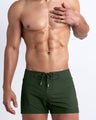 Frontal view of sexy model wearing the ALPHA GREEN men’s all-purpose swimwear bottoms in a forest green color by the Bang! brand of men's beachwear from Miami.