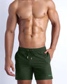 Frontal view of sexy model wearing the ALPHA GREEN men’s all-purpose swimwear bottoms in a forest green color by the Bang! brand of men's beachwear from Miami.