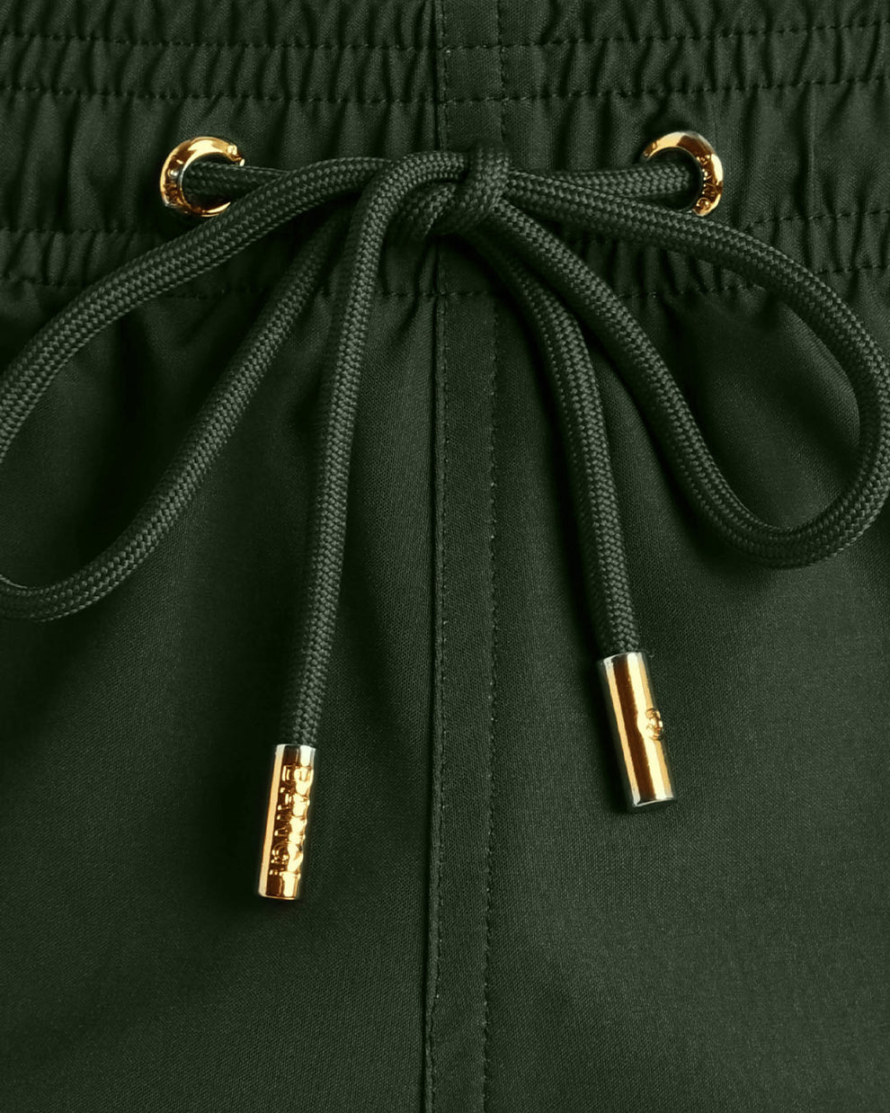 Close-up view of inseam and details of these shorts for men, with green cord and custom branded golden cord-ends, and matching custom eyelet trims in gold.