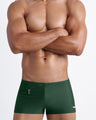Frontal view of a sexy male model wearing men’s swimsuit made with Italian-made Vita By Carvico Econyl Nylon with mini pocket in dark green color by the Bang! Menswear brand from Miami.