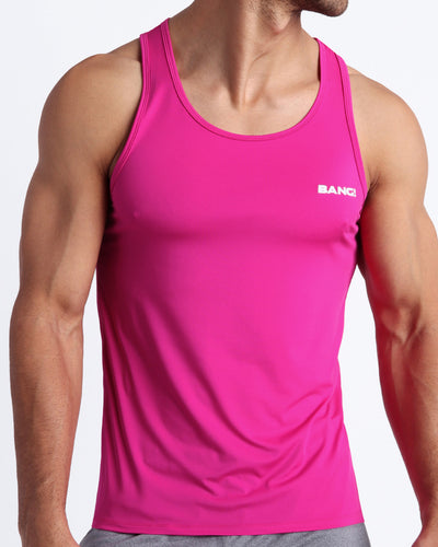 Frontal view of male model wearing the CONFESS MAGENTA in a solid pink gym tank top for men by the Bang! brand of men's beachwear from Miami.