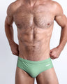 Frontal view of a sexy male model wearing the CABANA GREEN Swim Brief men’s swimsuit in a pastel green color made with Italian-made Vita By Carvico Econyl Nylon by the Bang! Menswear brand from Miami.