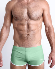 Frontal view of a sexy male model wearing the CABANA GREEN men’s swimsuit in a solid pastel green color by the Bang! Menswear brand from Miami.