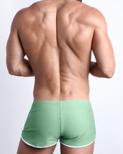 Back view of a male model wearing CABANA GREEN men’s swim shorts in a solid light green color made with Italian-made Vita By Carvico Econyl Nylon by the Bang! Clothes brand of men's beachwear.