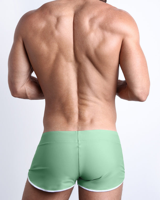 Back view of a male model wearing CABANA GREEN men’s swim shorts in a solid light green color by the Bang! Clothes brand of men&