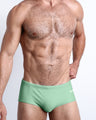 Frontal view of a sexy male model wearing men’s Brazilian style swimsuit in CABANA GREEN a light green color made with Italian-made Vita By Carvico Econyl Nylon by the Bang! Menswear brand from Miami.