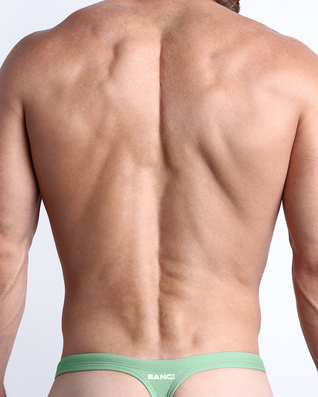 Back view of a male model wearing men’s CABANA GREEN swim thong in green color made with Italian-made Vita By Carvico Econyl Nylon with official logo of BANG! Brand in white.