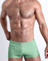 Frontal view of a sexy male model wearing men’s CABANA GREEN swimsuit with mini pockets in a light green color made with Italian-made Vita By Carvico Econyl Nylon by the Bang! Menswear brand from Miami.