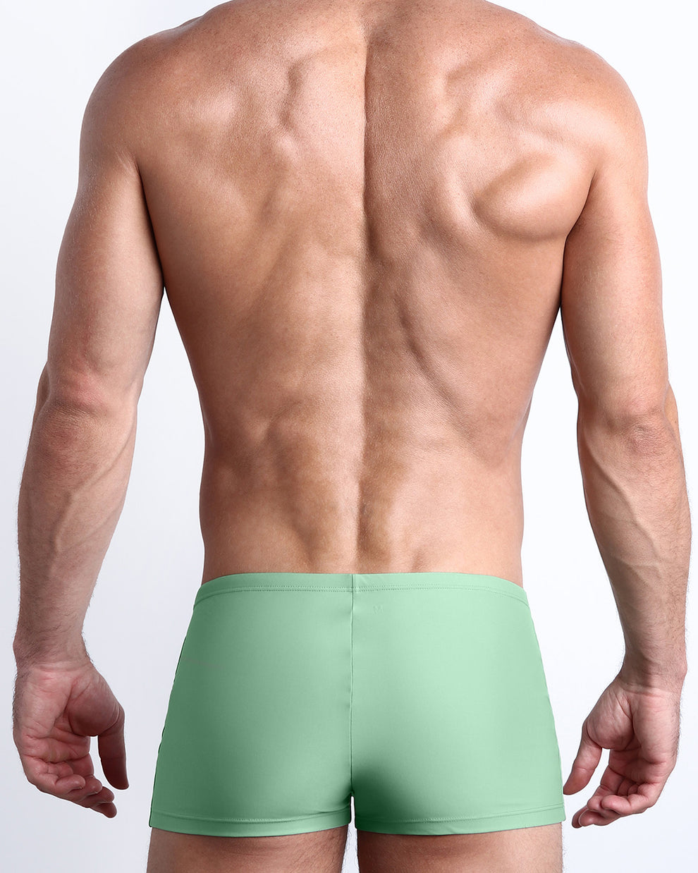 Back view of a male model wearing the CABANA GREEN men’s swim trunks in a solid green moss color made with Italian-made Vita By Carvico Econyl Nylon by the Bang! Clothes brand of men's beachwear from Miami.