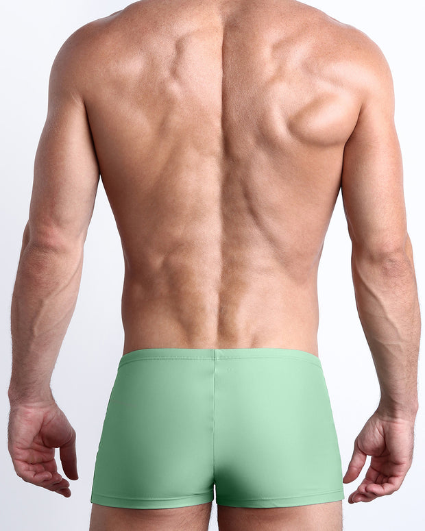 Back view of a male model wearing the CABANA GREEN men’s swim trunks in a solid green moss color made with Italian-made Vita By Carvico Econyl Nylon by the Bang! Clothes brand of men&