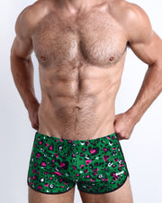 Frontal view of a sexy male model wearing men’s CAMO CHAMELEON swimsuit in a forest green color with white and pink camo print by the Bang! Menswear brand from Miami.