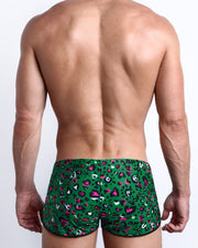 Back view of a male model wearing CAMO CHAMELEON men’s swim shorts featuring in teal with pink and black animal concealed print by the Bang! Clothes brand of men's beachwear.