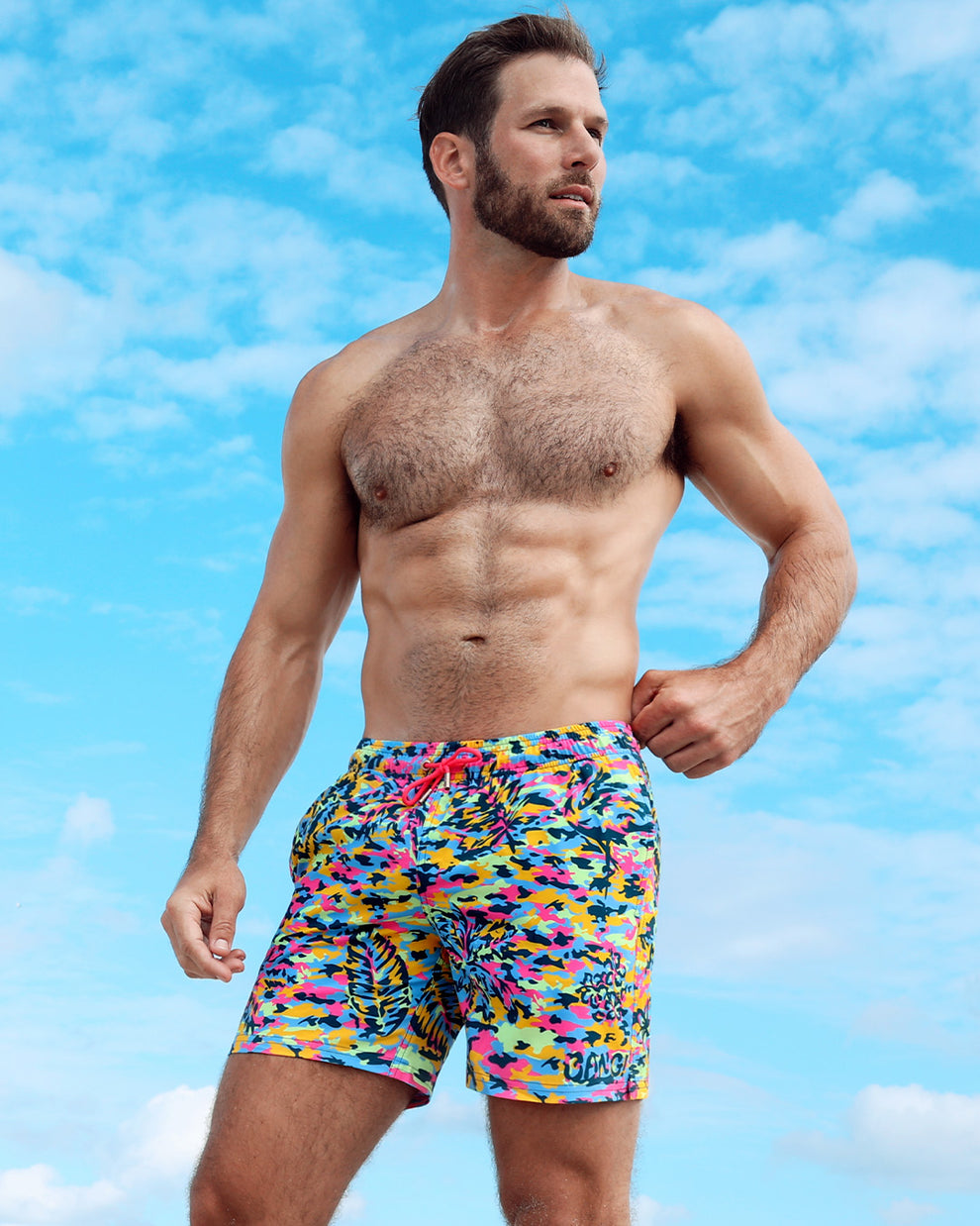 Male model in Camo Pop (neon mix) resort shorts by BANG! Clothes — vibrant camouflage pattern in neon colors with tropical leaf details, made for bold summer looks.