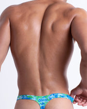 Back view of a model wearing CAMO POP (BLUE/GREEN) men’s beach swim thong featuring a colorful camo design with a burst of colors including blue and green made by the Bang! Miami official brand of men's swimwear.