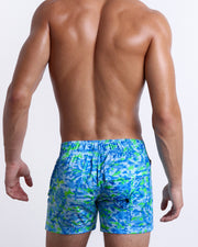 Male model wearing men’s CAMO POP (BLUE/GREEN) Flex Shorts swimsuit in a colorful blue and green neon camo print, complete with a back pocket, designed by BANG! Clothes in Miami.