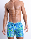 Male model wearing CAMO POP (BLUE/GREEN), a multicolor neon print for men. These premium quality swimwear bottoms are by BANG! Clothes, a men’s beachwear brand from Miami.