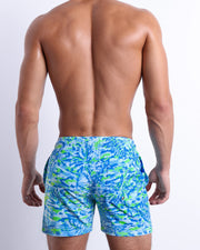 Male model wearing men’s CAMO POP (BLUE/GREEN) beach Resort Shorts swimsuit in a colorful blue and green neon camo print is designed by BANG! Clothes in Miami.
