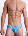 Front view of the CAMO POP (BLUE/GREEN) men’s bikini-style bottoms featuring a multicolor neon camo print, including shades of light blue, lime green, and blue colors. This premium quality swimwear is by BANG! Clothes, a men’s beachwear brand from Miami.