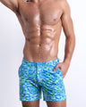 Front view of a male model wearing the men’s CAMO POP (BLUE/GREEN) Tailored Shorts, a multicolor neon print for men. These premium quality swimwear bottoms are by BANG! Clothes, a men’s beachwear brand from Miami.