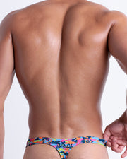 Back view of a model wearing CAMO POP (COLOR MIX) men’s beach swim thong featuring a colorful camo design with a burst of colors including blue, green, hot pink and orange colors made by the Bang! Miami official brand of men's swimwear.