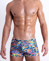 Front view of model wearing the CAMO POP (COLOR MIX) men’s bikini-style Swim Trunks, featuring a multicolor neon camo print, including shades of light blue, pink, lime green, and orange colors. These high-quality swimwear are by BANG!, a men’s beachwear brand from Miami.