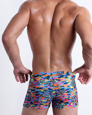 Back view of male model wearing the CAMO POP (COLOR MIX) beach sexy swimming bottoms for men in a colorful camo design with a burst of colors including blue and green, designed by BANG!.