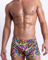 Male model wearing CAMO POP (NEON MIX) square leg swim shorts, a multicolor neon print for men. These premium quality swimwear bottoms are by BANG! Clothes, a men’s beachwear brand from Miami.