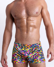 Male model wearing CAMO POP (NEON MIX) square leg swim shorts, a multicolor neon print for men. These premium quality swimwear bottoms are by BANG! Clothes, a men’s beachwear brand from Miami.