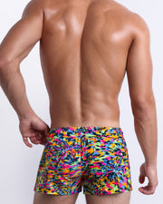 Male model wearing men’s CAMO POP (NEON MIX) beach Mini Shorts swimsuits in a colorful neon camo print, complete with zippered back pocket, are designed by BANG! Clothes in Miami.