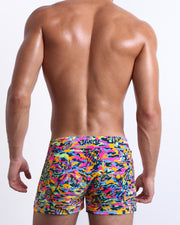 Male model wearing men’s CAMO POP (NEON MIX) Beach Shorts swimsuit in a colorful neon camo print, complete with a back pocket, designed by BANG! Clothes in Miami.