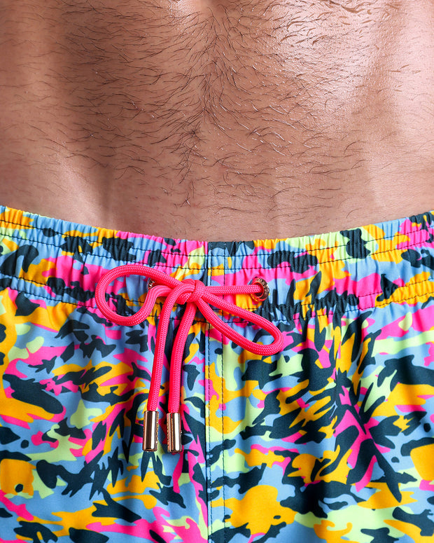 Close-up view of inseam and details of CAMO POP (NEON MIX) swimsuit for men, with hot pink cord and custom branded golden cord-ends, and matching custom eyelet trims in gold. 