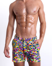 Male model wearing CAMO POP (NEON MIX) Tailored Shorts, a multicolor neon print for men. These premium quality swimwear bottoms are by BANG! Clothes, a men’s beachwear brand from Miami.