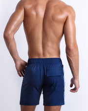 Back view of male model wearing men’s CASINO ROYALE (BLUE) beach Flex Boardshorts swimming shorts in a blue color. Inspired by actor Daniel Craig's iconic blue swim trunks worn in the 2006 film Casino Royale, are designed by BANG! Clothes in Miami.
