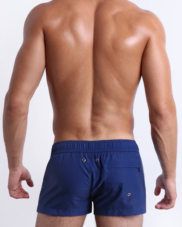 Back view of male model wearing men’s CASINO ROYALE (BLUE) beach Resort Shorts swimsuits in a blue color. Inspired by actor Daniel Craig&