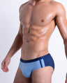 Side view of muscular male model wearing CASINO ROYALE (BLUE) Summer swim brief swimsuit for the beach with a stylish color block design in dark blue for men. This high-quality brief is by BANG! Clothes, a men’s beachwear brand from Miami. Inspired by the iconic style of Daniel Craig's blue swim trunks in the 2006 film Casino Royale.